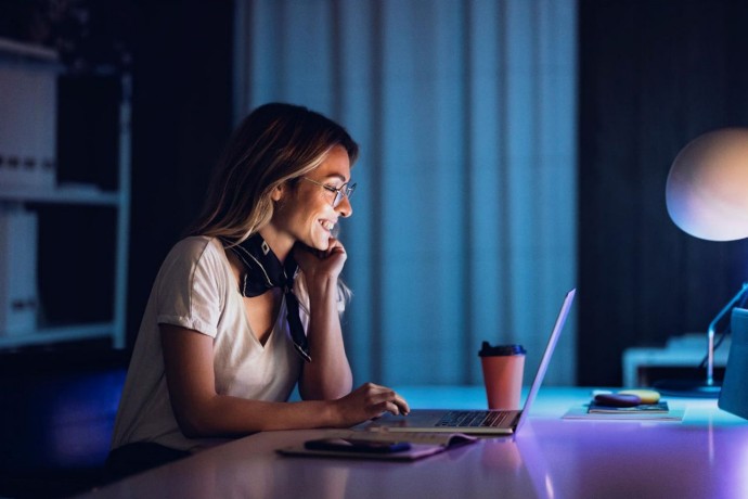 Cheerful lady with coffee and laptop in night